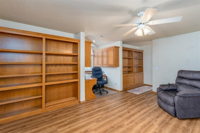 office with a textured ceiling, built in desk, light hardwood / wood-style flooring, and ceiling fan