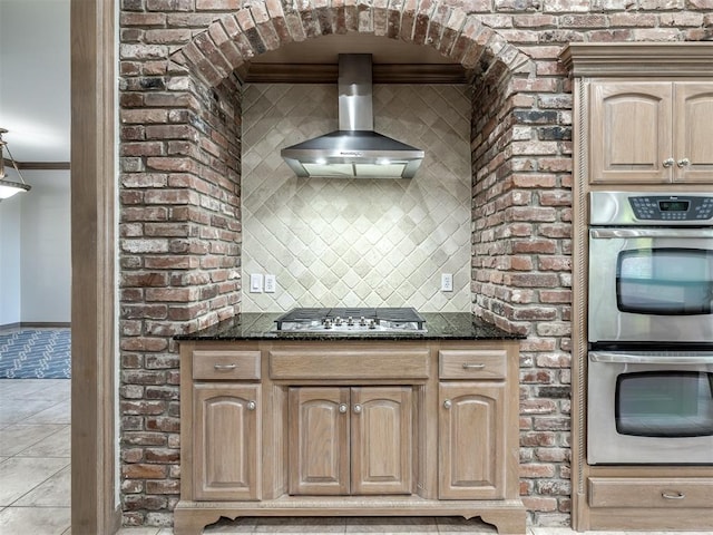 kitchen with crown molding, wall chimney exhaust hood, dark stone counters, and appliances with stainless steel finishes