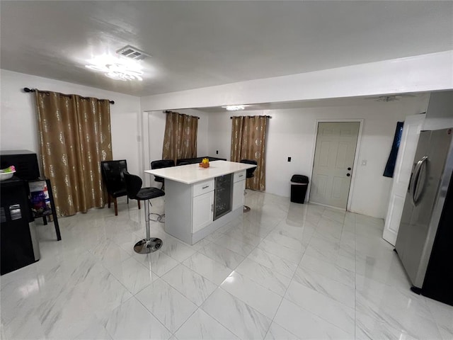 kitchen with a breakfast bar, a center island, white cabinetry, and stainless steel refrigerator