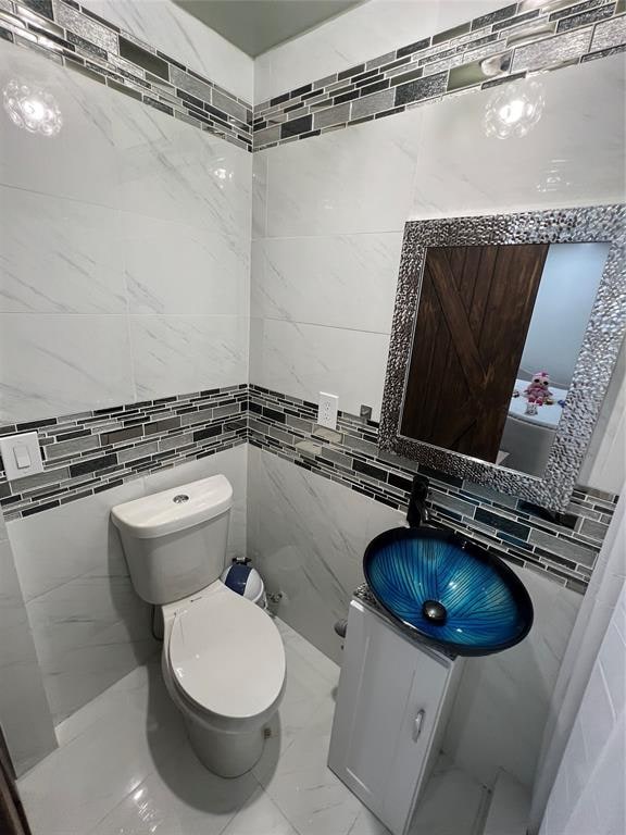 bathroom with vanity, toilet, and tile walls