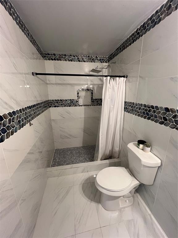 bathroom with a shower with shower curtain, toilet, and tile walls