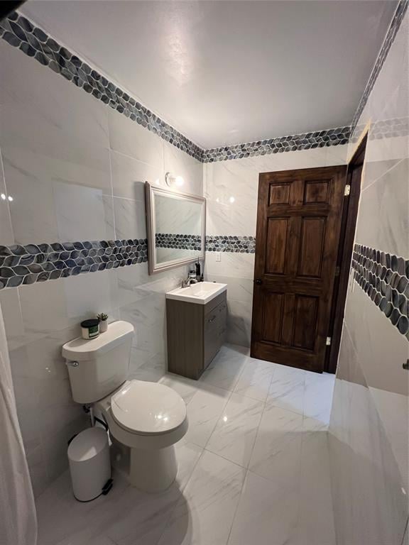 bathroom with vanity, tile walls, and toilet