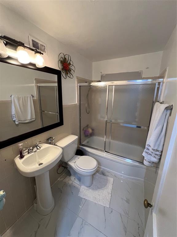 bathroom featuring bath / shower combo with glass door, tile walls, and toilet