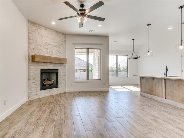 unfurnished living room with ceiling fan, a stone fireplace, sink, and light hardwood / wood-style flooring