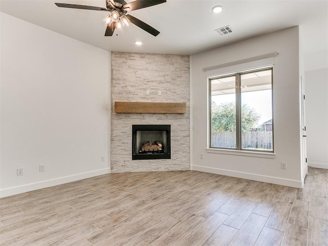 unfurnished living room with light wood-type flooring, a stone fireplace, and ceiling fan