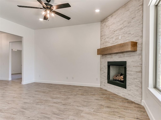 unfurnished living room featuring ceiling fan, a stone fireplace, and light wood-type flooring