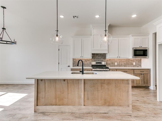 kitchen with white cabinetry, sink, pendant lighting, a center island with sink, and appliances with stainless steel finishes