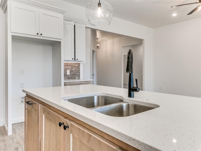 kitchen featuring light stone counters, sink, light hardwood / wood-style flooring, white cabinets, and hanging light fixtures