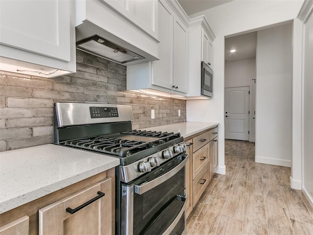 kitchen featuring custom exhaust hood, white cabinets, light stone countertops, light hardwood / wood-style floors, and stainless steel appliances