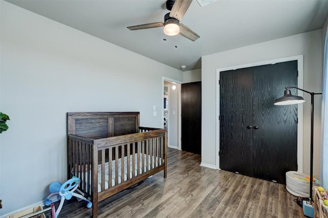 bedroom with hardwood / wood-style flooring, ceiling fan, and a crib