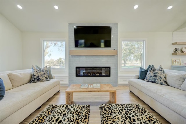 living room with a large fireplace, light hardwood / wood-style flooring, and vaulted ceiling