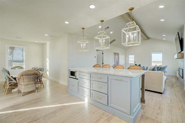 kitchen featuring a center island, lofted ceiling with beams, gray cabinets, light wood-type flooring, and decorative light fixtures