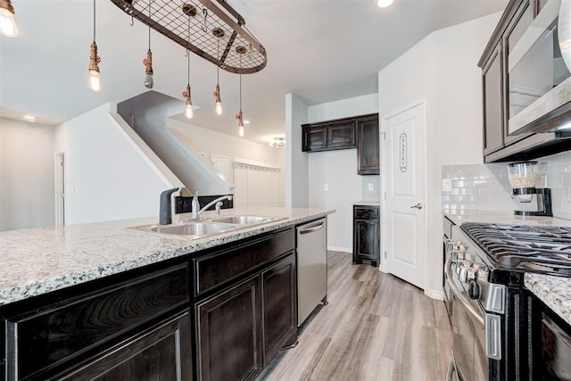 kitchen with appliances with stainless steel finishes, decorative backsplash, pendant lighting, light hardwood / wood-style flooring, and sink