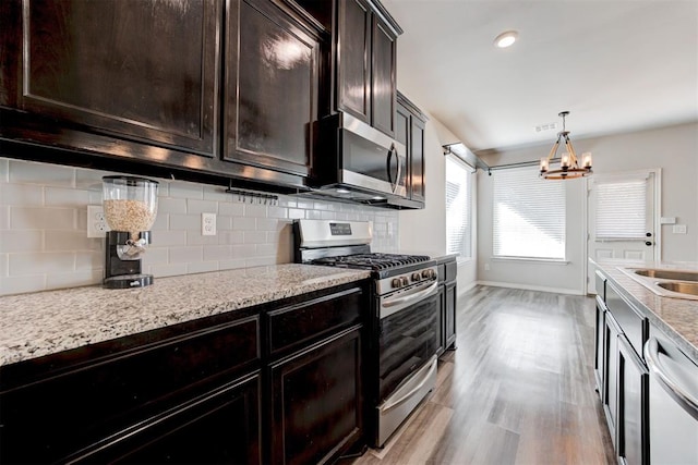 kitchen featuring light hardwood / wood-style floors, stainless steel appliances, tasteful backsplash, hanging light fixtures, and a chandelier