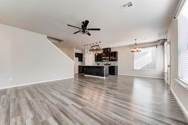 unfurnished living room featuring ceiling fan with notable chandelier and hardwood / wood-style flooring