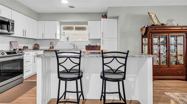 kitchen featuring a center island, light hardwood / wood-style flooring, light stone countertops, white cabinetry, and stainless steel appliances