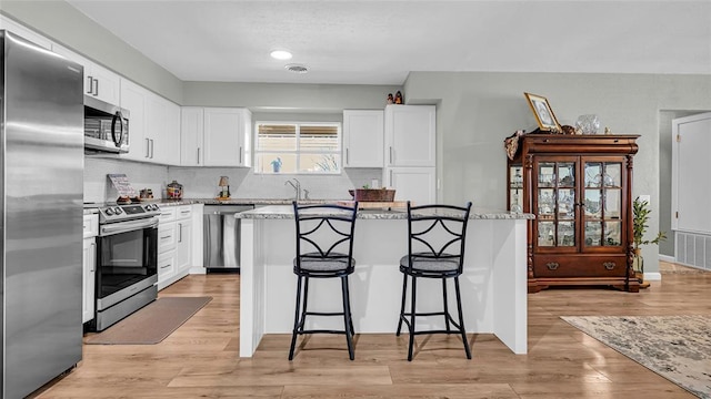 kitchen with light stone countertops, stainless steel appliances, a center island, light hardwood / wood-style floors, and white cabinetry