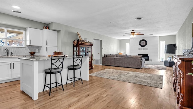 kitchen featuring white cabinets, light stone counters, light wood-type flooring, and a brick fireplace