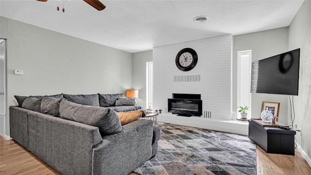 living room with a brick fireplace, ceiling fan, and hardwood / wood-style flooring