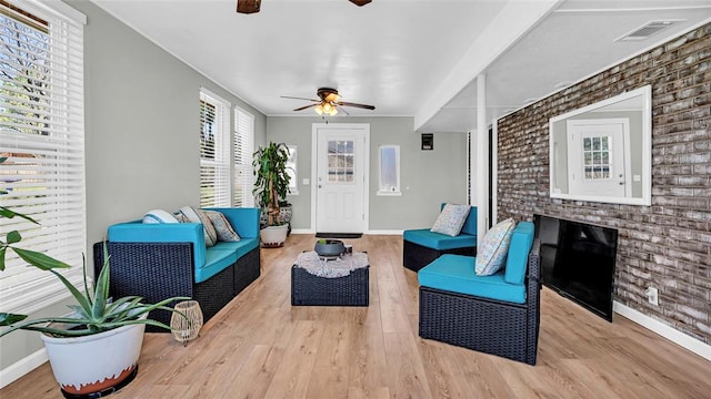 living room with ceiling fan, light hardwood / wood-style flooring, a wealth of natural light, and brick wall