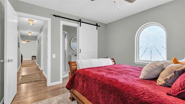 bedroom with a barn door, ceiling fan, light hardwood / wood-style flooring, and multiple windows