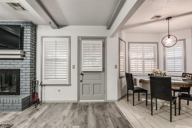 entrance foyer with beam ceiling, a fireplace, a textured ceiling, and light hardwood / wood-style floors