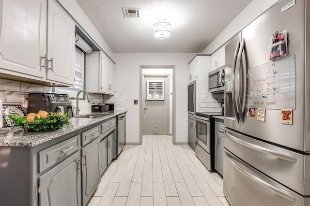 kitchen featuring sink, appliances with stainless steel finishes, light stone counters, white cabinets, and decorative backsplash