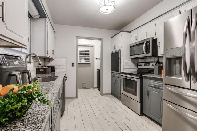 kitchen featuring appliances with stainless steel finishes, white cabinetry, sink, decorative backsplash, and light stone counters