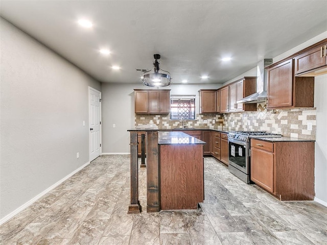 kitchen featuring backsplash, wall chimney range hood, sink, stainless steel gas stove, and a kitchen island