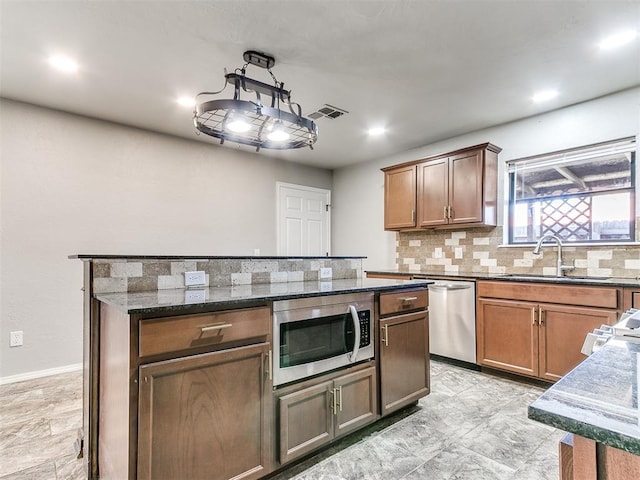 kitchen with appliances with stainless steel finishes, tasteful backsplash, dark stone counters, sink, and a center island