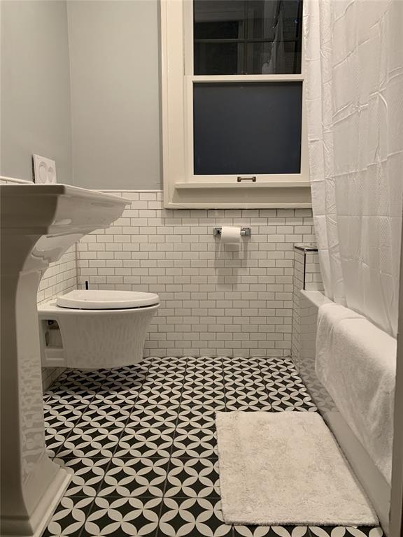 bathroom featuring toilet, shower / bathtub combination with curtain, and tile walls