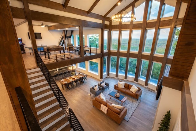 living room with beam ceiling, ceiling fan with notable chandelier, hardwood / wood-style flooring, and high vaulted ceiling