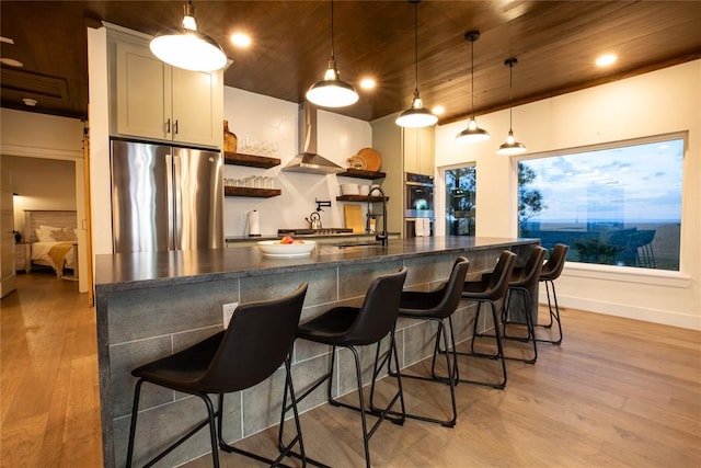 kitchen featuring a kitchen bar, light hardwood / wood-style floors, stainless steel refrigerator, and wall chimney exhaust hood