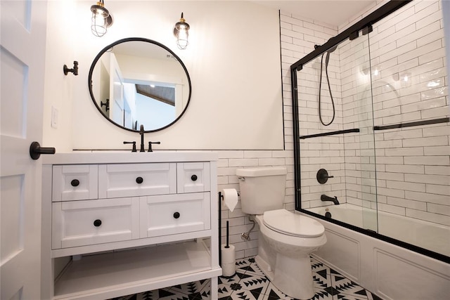 full bathroom with vanity, shower / bath combination with glass door, tile patterned flooring, toilet, and tile walls