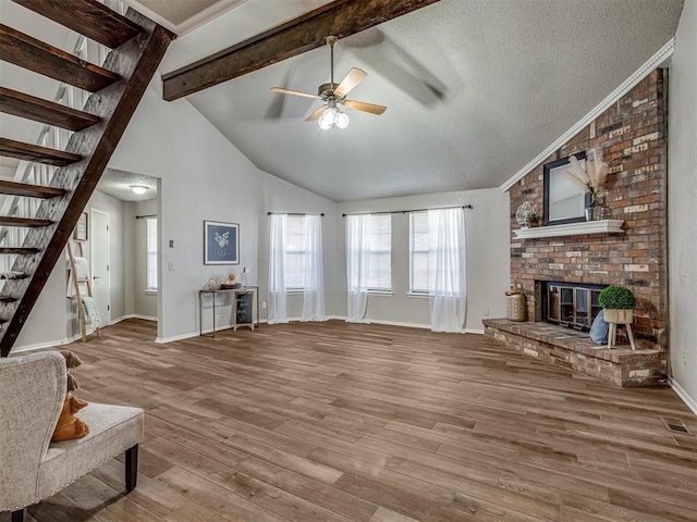 unfurnished living room featuring a textured ceiling, ceiling fan, beamed ceiling, a fireplace, and hardwood / wood-style floors