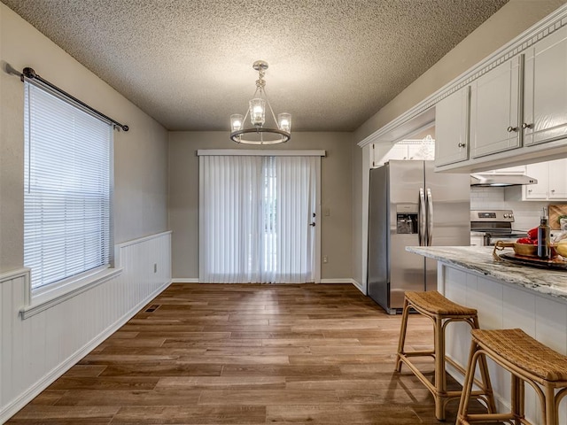 kitchen with an inviting chandelier, white cabinets, appliances with stainless steel finishes, light stone counters, and wood-type flooring