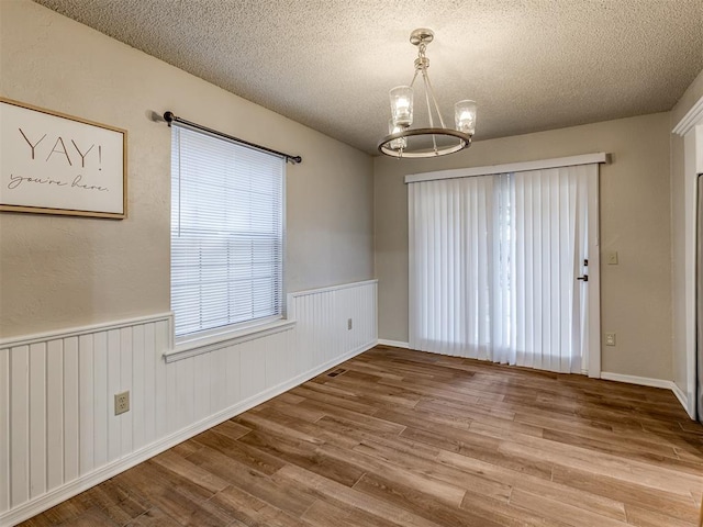 unfurnished dining area featuring hardwood / wood-style floors, a notable chandelier, and a textured ceiling