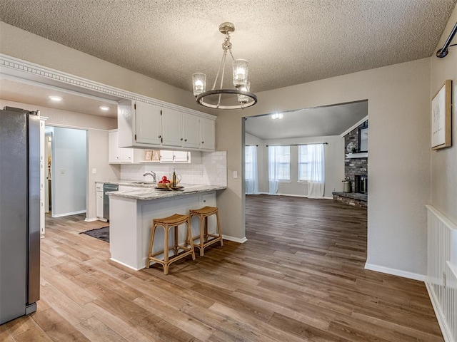 kitchen with kitchen peninsula, a kitchen bar, light wood-type flooring, stainless steel appliances, and white cabinetry