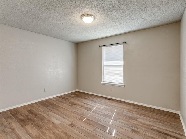 empty room with light wood-type flooring and a textured ceiling