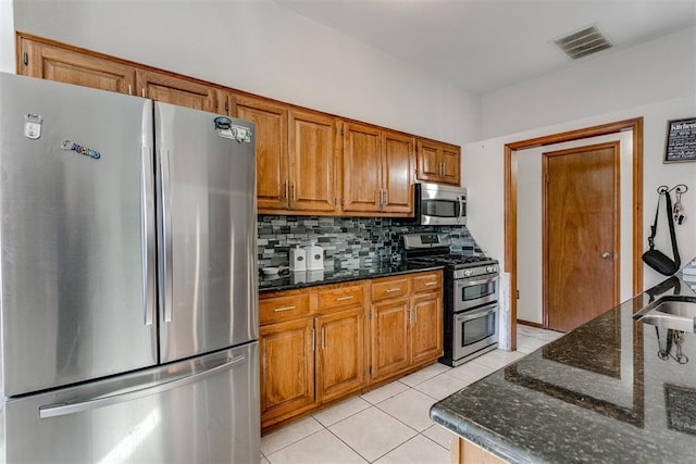 kitchen featuring decorative backsplash, appliances with stainless steel finishes, light tile patterned flooring, and dark stone countertops