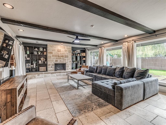 living room with ceiling fan, built in features, beamed ceiling, a textured ceiling, and a fireplace