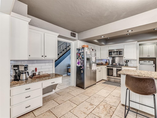 kitchen with stone countertops, white cabinetry, backsplash, and appliances with stainless steel finishes