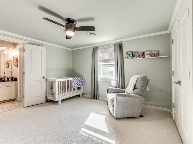 bedroom featuring a crib, carpet flooring, ensuite bathroom, and ceiling fan