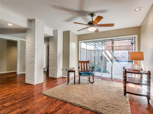 living area featuring ornate columns, ceiling fan, and dark hardwood / wood-style flooring