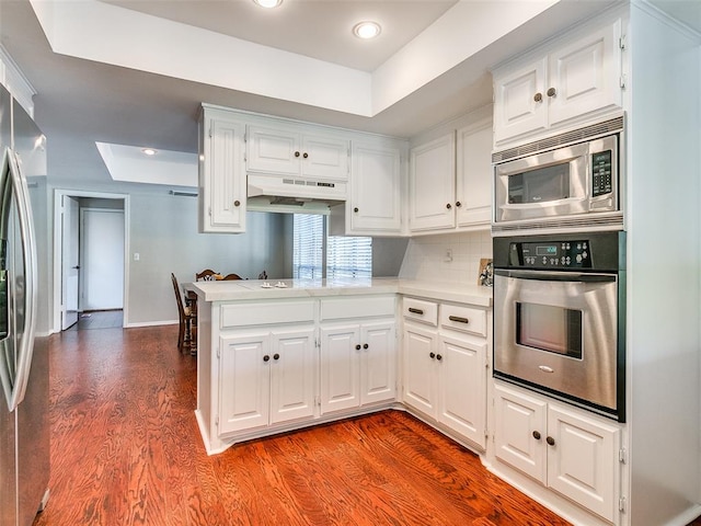 kitchen featuring kitchen peninsula, hardwood / wood-style floors, stainless steel appliances, and white cabinetry