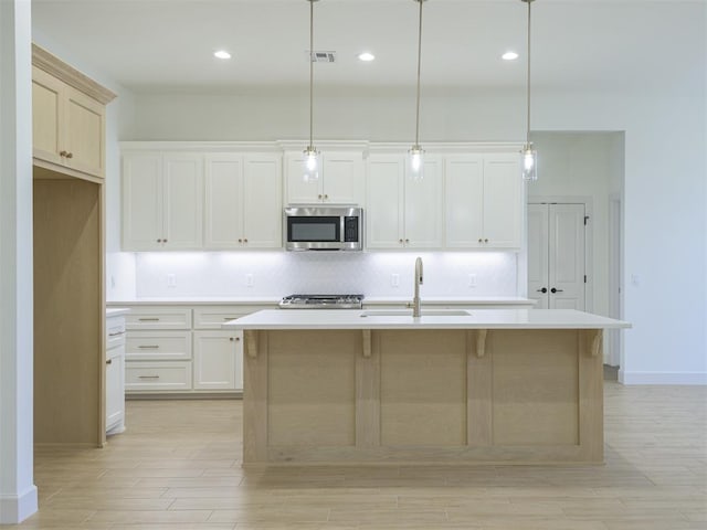 kitchen featuring appliances with stainless steel finishes, light wood-type flooring, sink, a center island with sink, and hanging light fixtures