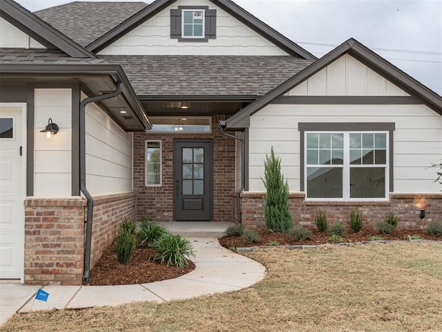 12129 SW 45th Ter, Mustang, OK 73064 - view of exterior entry with roof with shingles, brick siding, a yard, and board and batten siding