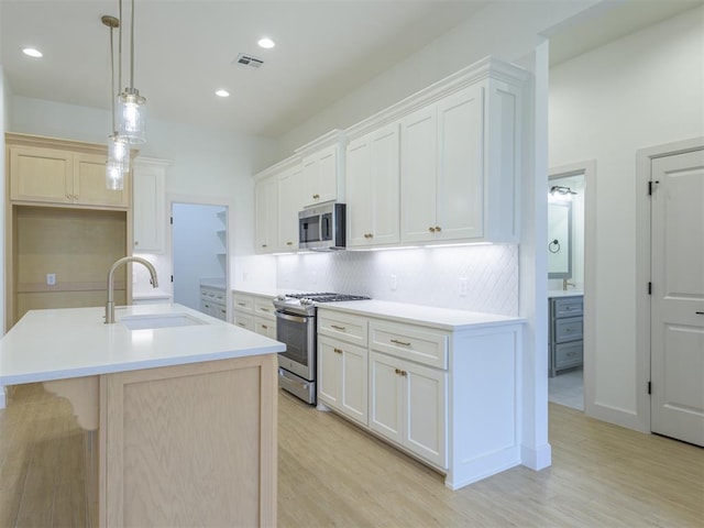 12129 SW 45th Ter, Mustang, OK 73064 - kitchen with appliances with stainless steel finishes, a sink, light wood-style flooring, decorative backsplash, and an island with sink