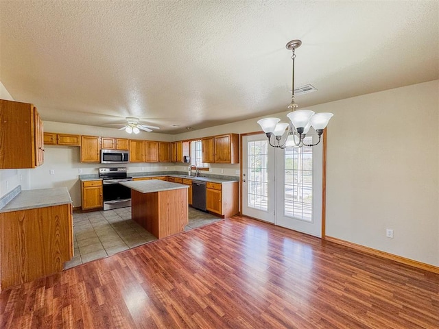 kitchen featuring sink, hanging light fixtures, light hardwood / wood-style flooring, a kitchen island, and appliances with stainless steel finishes