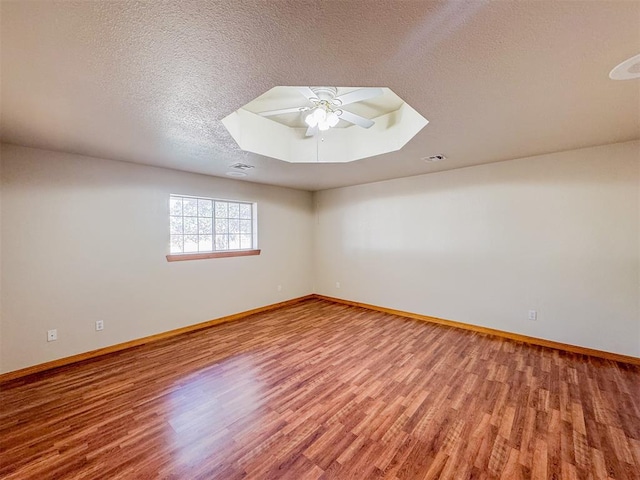 empty room featuring a textured ceiling, hardwood / wood-style flooring, a raised ceiling, and ceiling fan